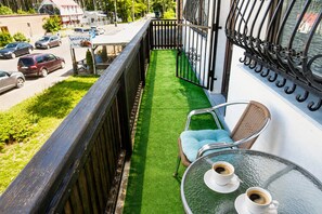 Ein Balkon mit künstlichem Rasen, einem Korbstuhl und einem Tisch mit zwei Tassen Kaffee.
