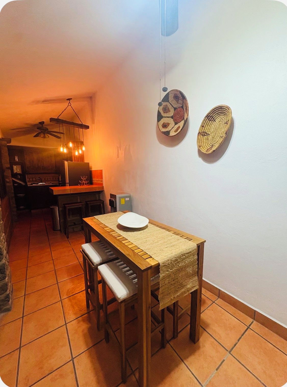 A dining area with a wooden table and chairs, a ceiling fan, and a wall-mounted light fixture.