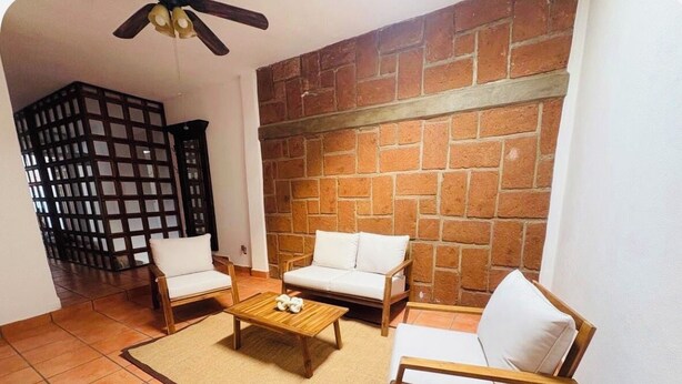 A living room with a brick wall, two white sofas, a wooden coffee table, and a ceiling fan.