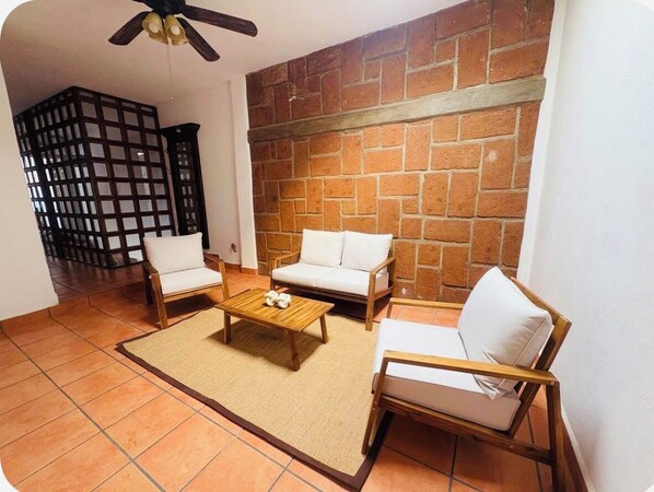 A living room with a brick wall, two white sofas, a wooden coffee table, and a ceiling fan.