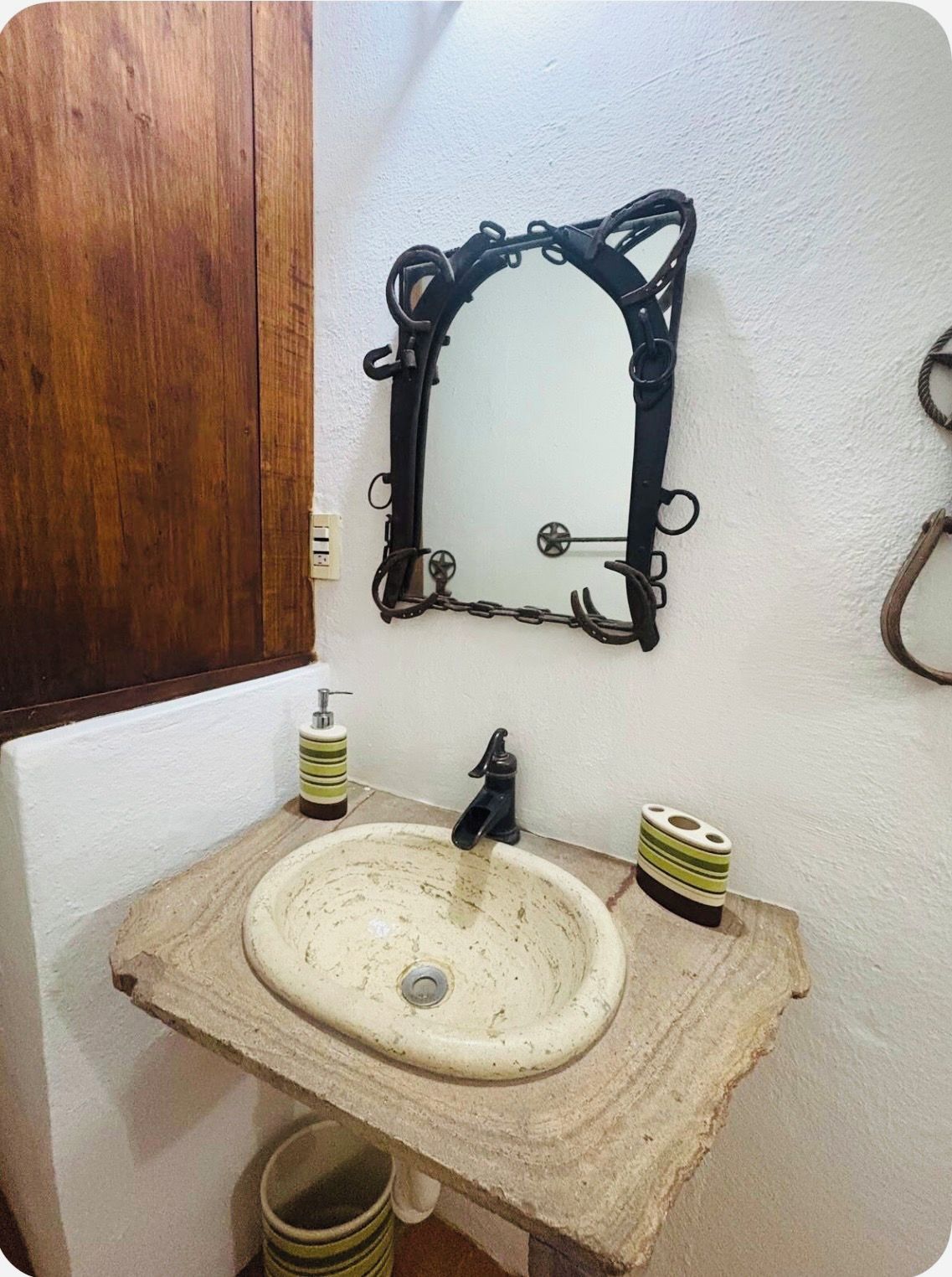 A bathroom with a wooden vanity, a white sink, a black faucet, and a mirror with a black ornate frame.