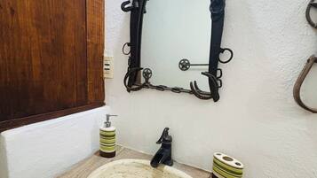 A bathroom with a wooden vanity, a white sink, a black faucet, and a mirror with a black ornate frame.