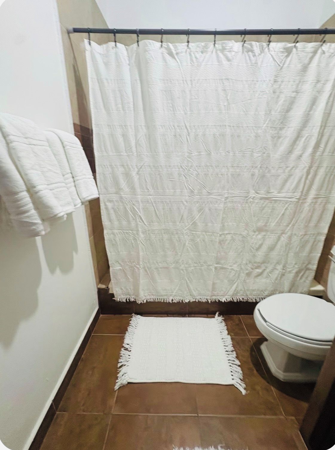 Un baño con cortina de ducha, una toalla blanca y un tapete en el suelo.