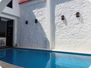 A swimming pool adjacent to a white textured wall with three wall-mounted light fixtures. - Alberca, Descanso, Encanto, Calidez y Tradición. Mascotas son Bienvenidas.  (Miacatlán)