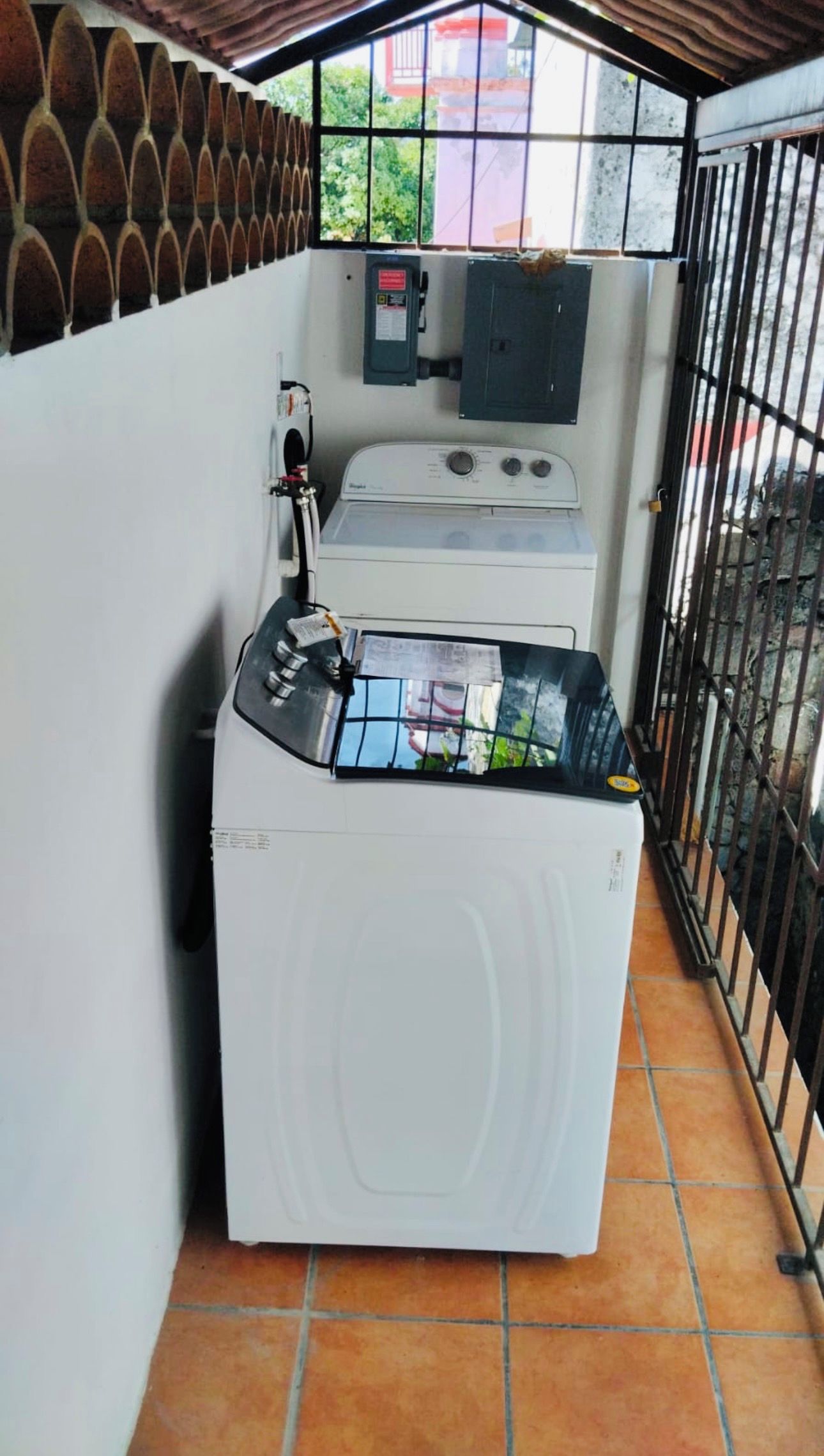 A compact laundry room with a washing machine, a utility meter, and a metal gate.
