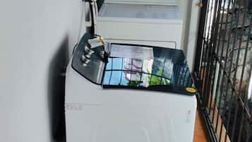 A compact laundry room with a washing machine, a utility meter, and a metal gate.