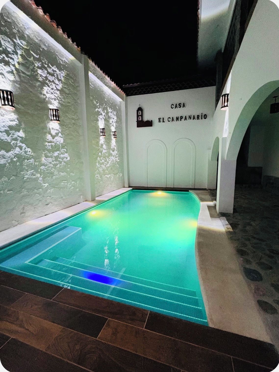 An indoor swimming pool with a tiled floor, surrounded by white walls and a sign reading 'CASA EL CAMPANARIO'.