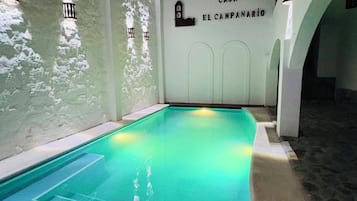 An indoor swimming pool with a tiled floor, surrounded by white walls and a sign reading 'CASA EL CAMPANARIO'.