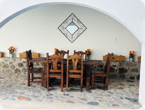 A stone-floored dining area with a wooden table and chairs, a decorative wall mirror, and potted plants. - Alberca, Descanso, Encanto, Calidez y Tradición. Mascotas son Bienvenidas.  (Miacatlán)