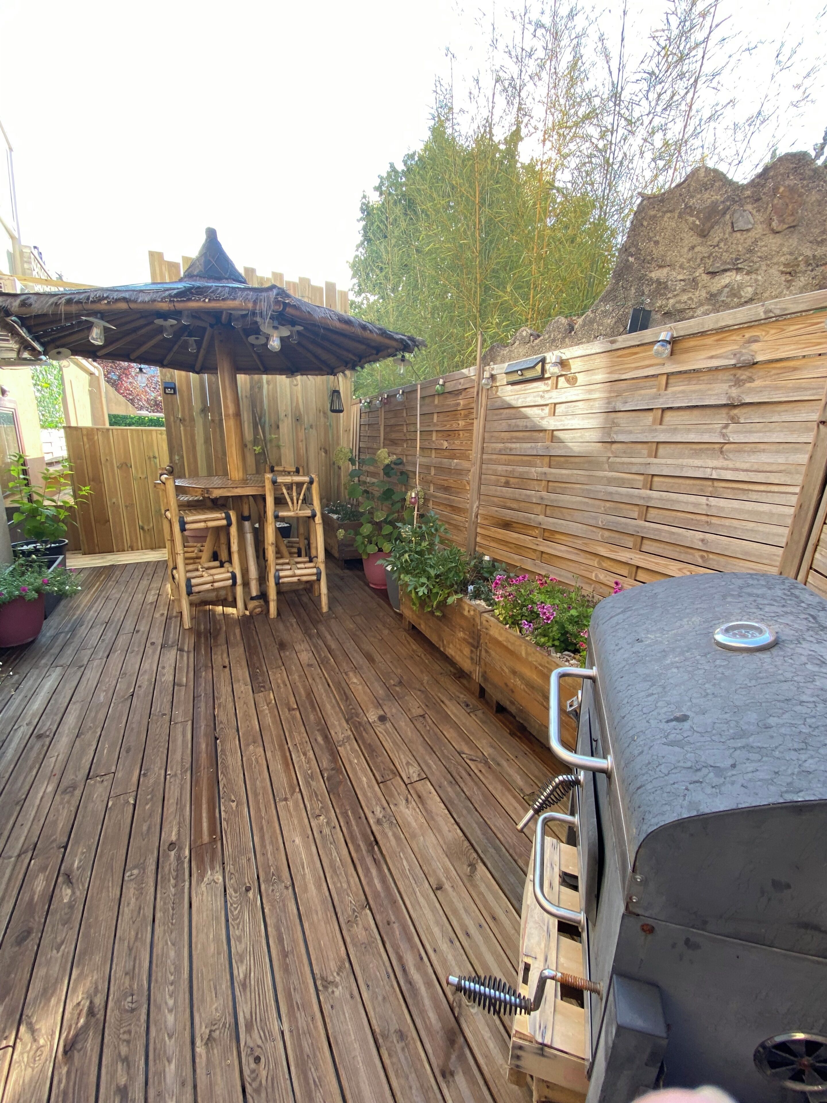 Una terraza de madera con una parrilla, una mesa y sillas de madera.