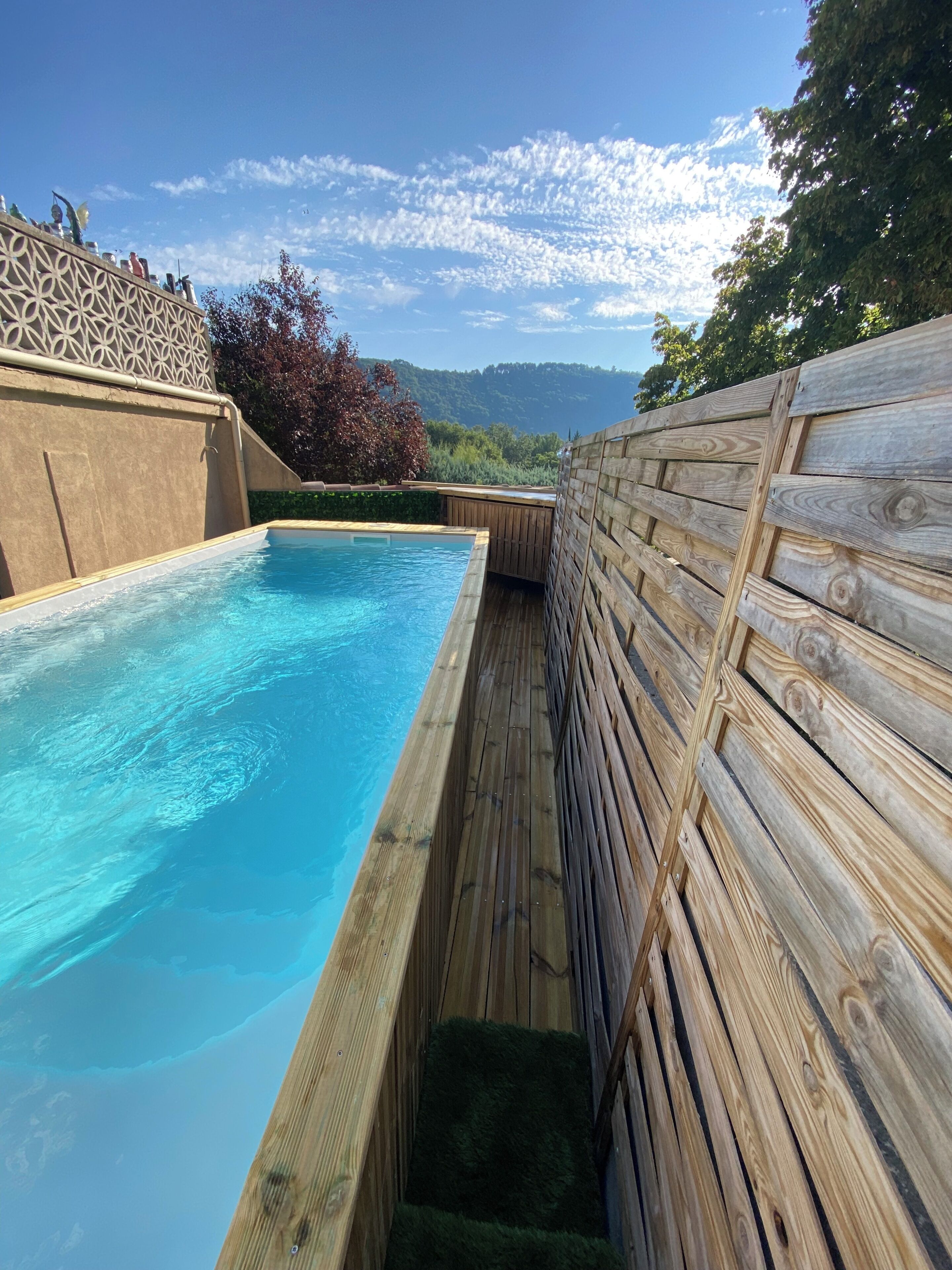 A rectangular pool with a wooden deck and a decorative fence.