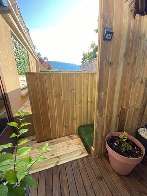 Una terrassa de fusta amb una tanca de fusta, una planta en test i una zona verda petita.