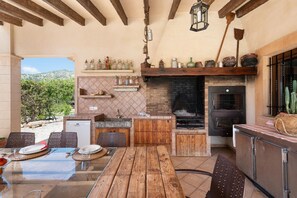 Une cuisine extérieure dotée d’une cheminée en briques, de meubles en bois et d’une table à manger pour quatre personnes.