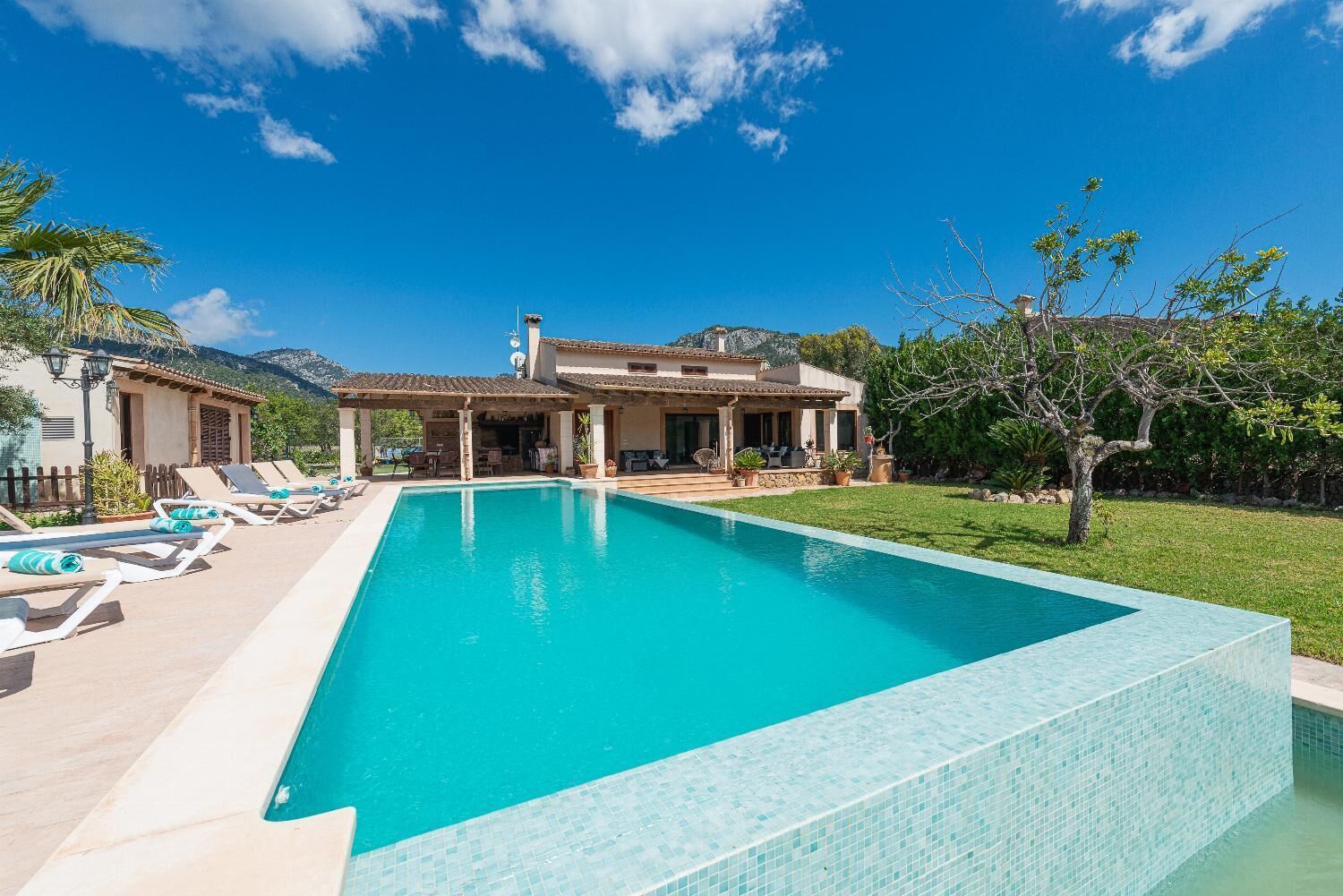 Una piscina rectangular con borde de azulejos, rodeada de sillones de descanso y un área de terraza cubierta.