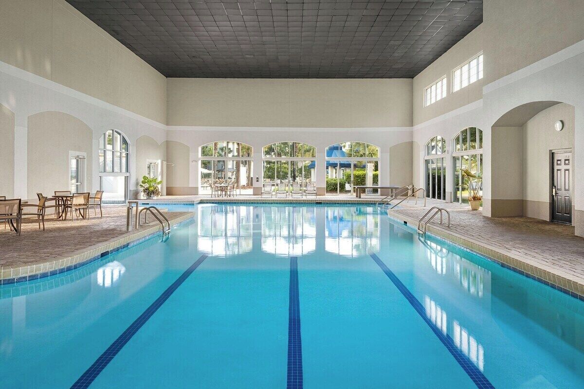 A large indoor swimming pool with clear blue water, surrounded by seating areas and large windows.