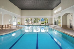 Una amplia piscina interior con agua cristalina y azul, rodeada de zonas de estar y grandes ventanales.