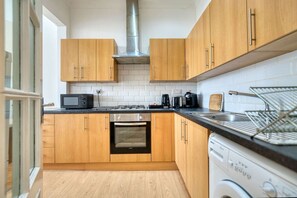 A modern kitchen with wooden cabinets, a stainless steel range hood, a microwave, a toaster, and a dishwasher. - Central Finnieston Tenement | Walk to Hydro (Finnieston)