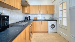 Een compacte keuken met houten kastjes, een gasfornuis, een koffiezetapparaat en een wasmachine.