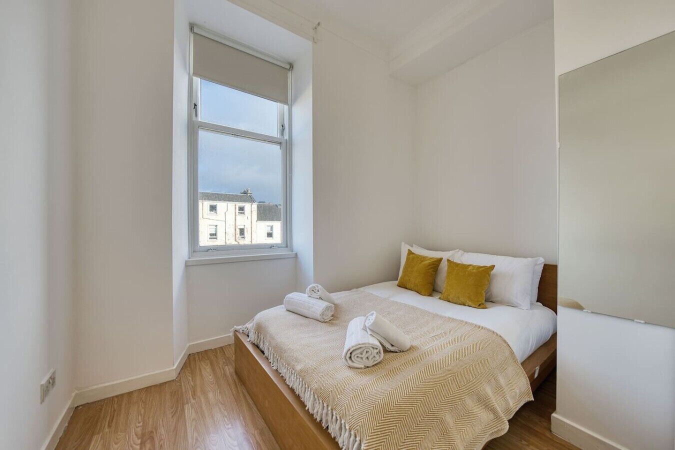 Quarto com cama, janela e vista para prédios.