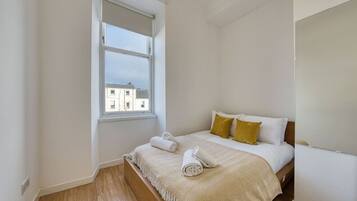 Quarto com cama, janela e vista para prédios.