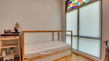 A room with a wooden bunk bed, a desk with a lamp, and a large window with a colorful stained glass design.