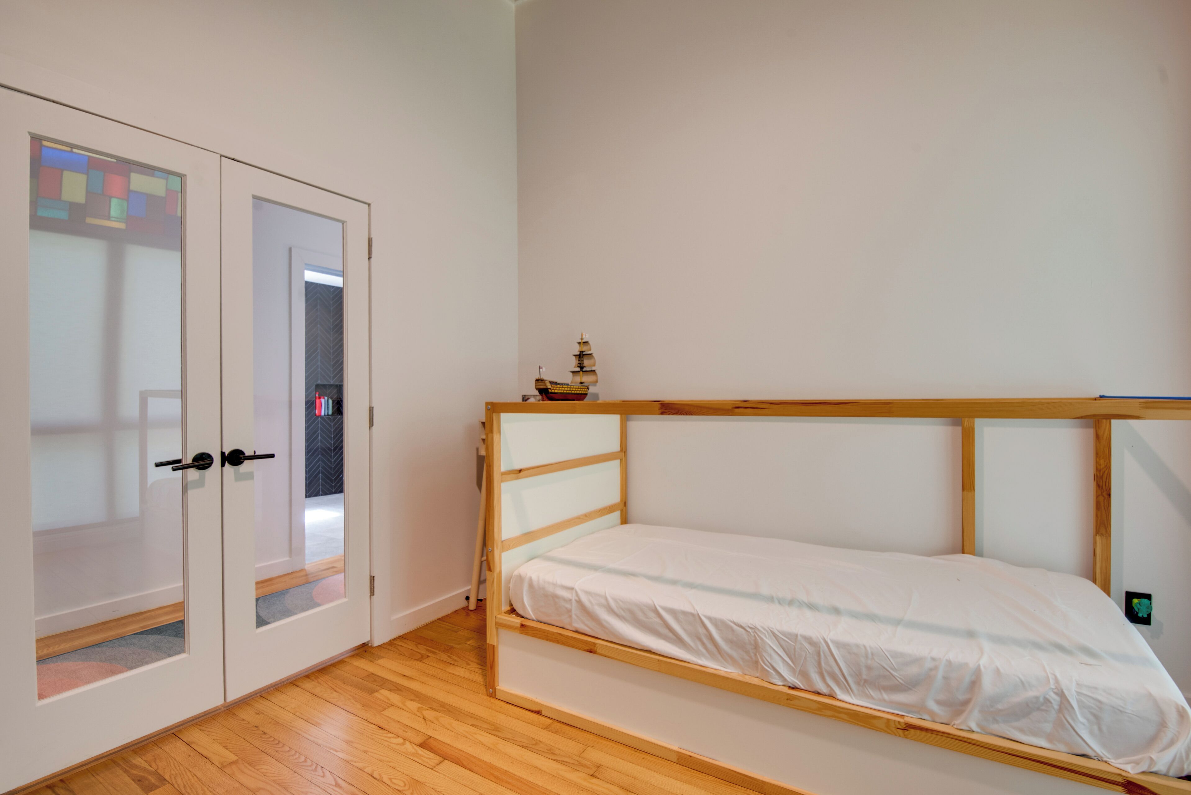 Un lit simple avec un cadre en bois et une literie blanche, dans une pièce au plancher et aux murs blancs, également en bois.