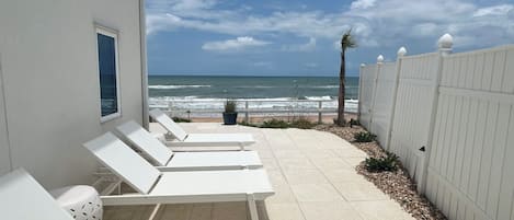 Une propriété située en bord de mer, avec des chaises longues blanches alignées le long d’une promenade pavée qui mène à l’océan.