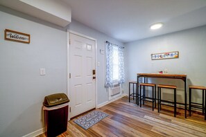 A hallway with a white door, a welcome sign, a radiator, a trash bin, and a bar area with stools.