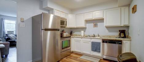 A modern kitchen with stainless steel appliances, white cabinetry, and a wooden floor.