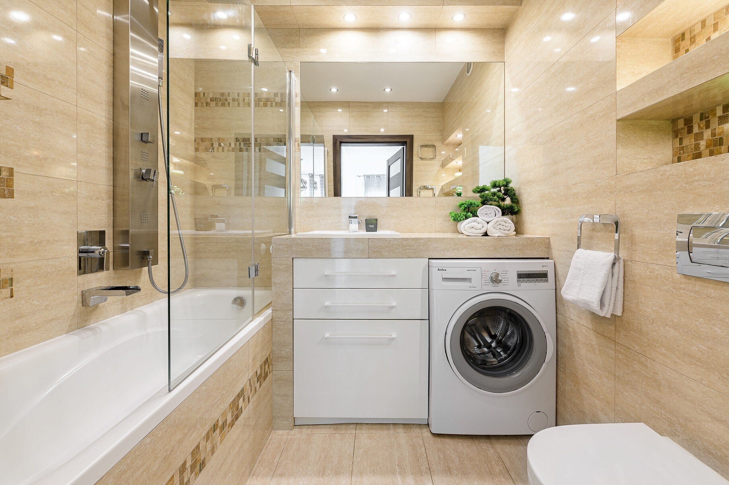 A modern bathroom with a glass-enclosed shower, a built-in washing machine, and a toilet.