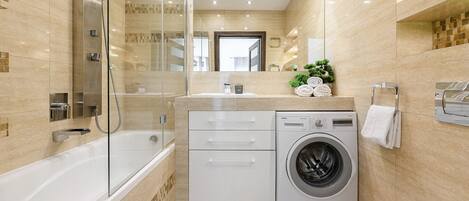 A modern bathroom with a glass-enclosed shower, a built-in washing machine, and a toilet.