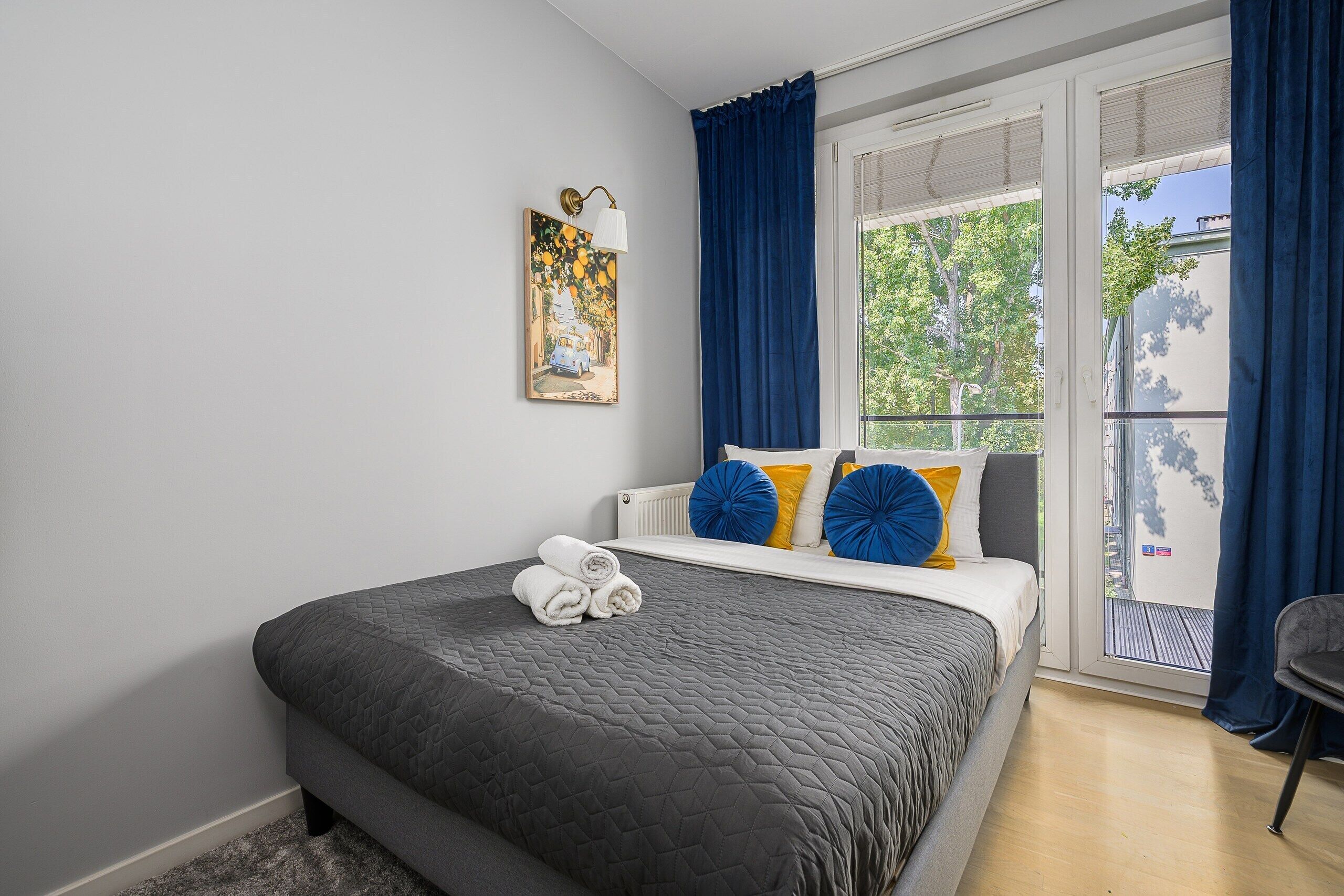 A bedroom with a bed, a window with curtains, a radiator, and a painting on the wall.