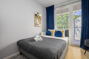 Un dormitorio con cama, ventana con cortinas, radiador y un cuadro en la pared.