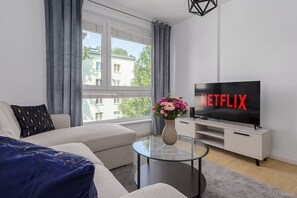 A modern living room with a sofa, a coffee table, a TV with 'NETFLIX' on the screen, and a window with curtains. - Lumina modern Apart parking 2 balcony (Warszawa)