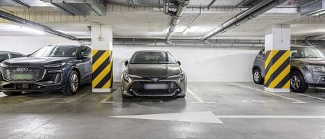 Un estacionamiento con tres coches aparcados en espacios designados, pilares de hormigón con franjas amarillas y negras y flechas direccionales en el suelo.