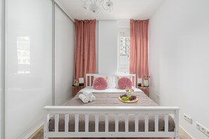 A neatly arranged bedroom with a bed, pillows, a bedside table, and a window with curtains. - Lumina modern Apart parking 2 balcony (Warszawa)