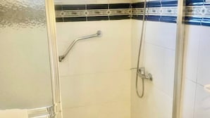 Un bagno con box doccia in vetro, pavimento in legno, lavandino bianco e finestra con persiane.