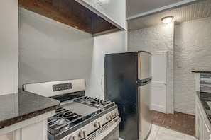 A compact kitchen with a gas stove, a refrigerator, and a white door. - Walk Everywhere! Monte Vista Apartment Near Cafes (San Antonio)