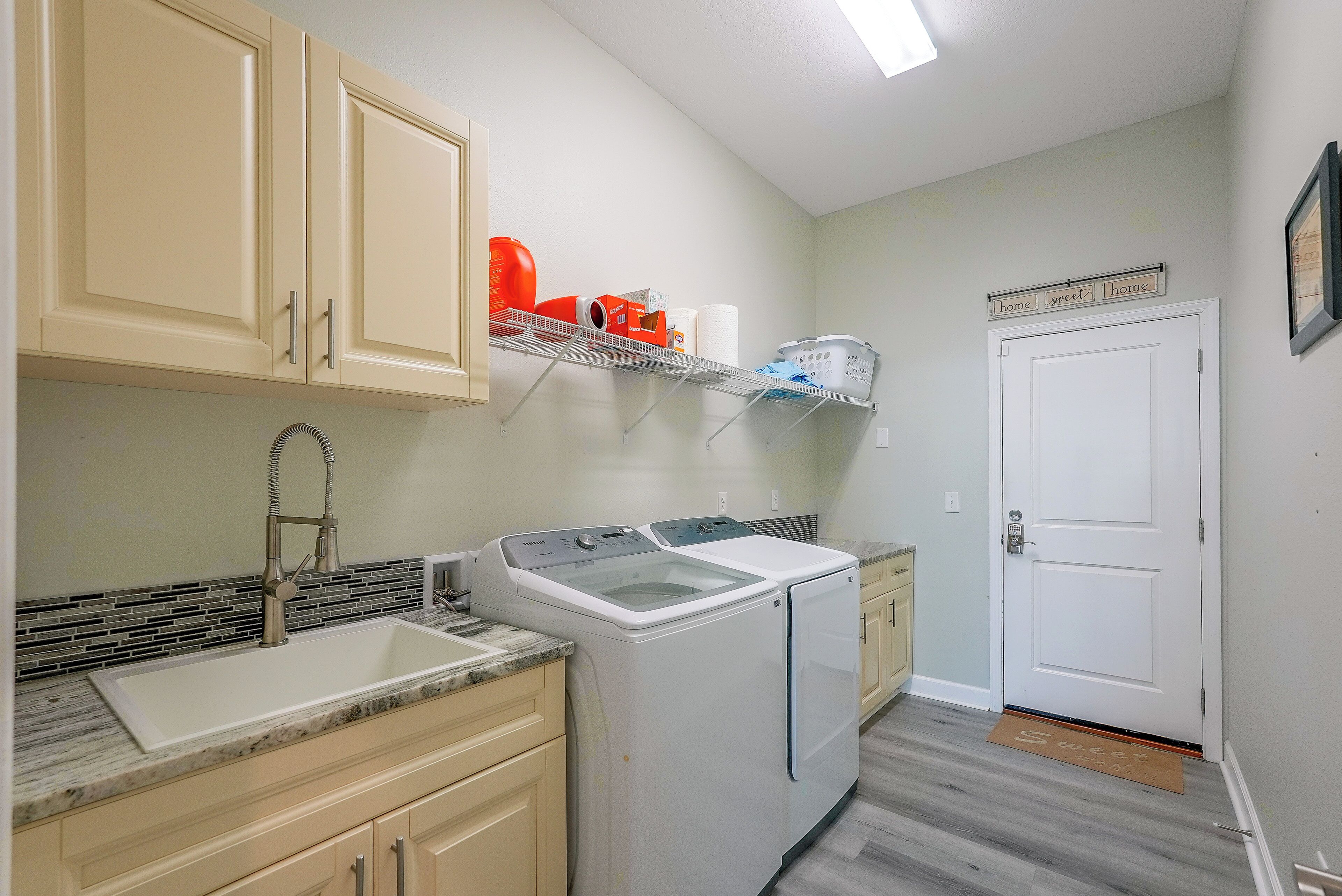 A laundry area with a washing machine, a sink, and a shelf with laundry supplies.