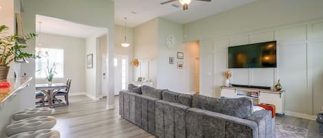 A spacious living area with a sectional sofa, a dining table, and a flat-screen TV mounted on the wall.