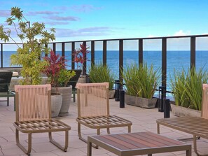 Ein Sitzbereich im Freien mit Stühlen und Tischen, Blumentöpfen und Blick auf das Meer.