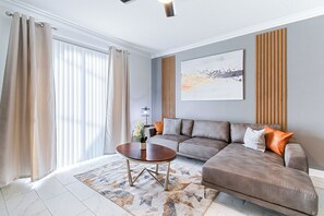 A modern living room with a sectional sofa, a coffee table, and a large abstract painting on the wall. - Special Offer! Cozy Townhome/Private Pool/Themed BRs 3011PL (Kissimmee)