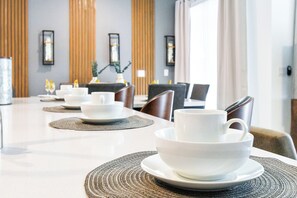 Un comedor con una mesa larga dispuesta para varias personas, con platos y cuencos blancos y un mantel individual tejido.