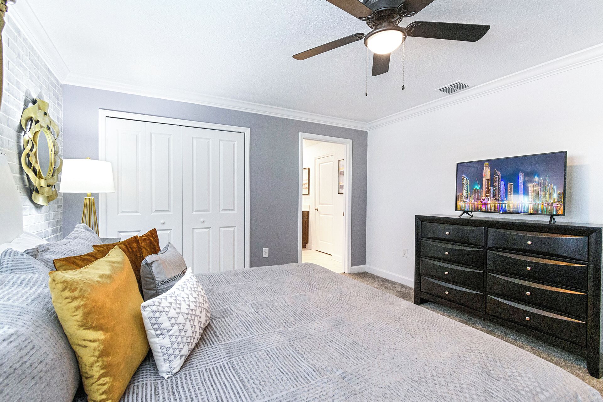 A bedroom with a bed, a dresser, a ceiling fan, and a cityscape painting on the wall.