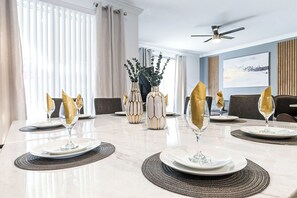 A dining area with a white table set for six, including wine glasses and plates, with a ceiling fan above. - Special Offer! Cozy Townhome/Private Pool/Themed BRs 3011PL (Kissimmee)