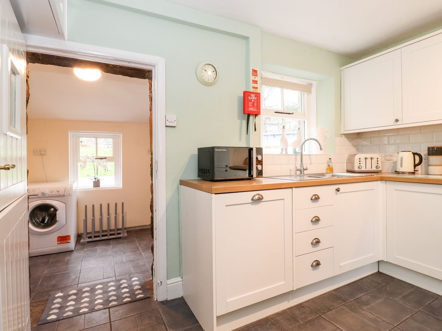 A compact kitchen with white cabinets, a microwave, a toaster, and a kettle.