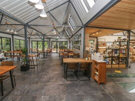 A spacious cafe with multiple tables and chairs, a counter with various items, and large windows allowing natural light.