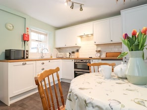 A kitchen with white cabinets, a microwave, a toaster, and a table with a floral tablecloth. - Irt Cottage (Seascale)