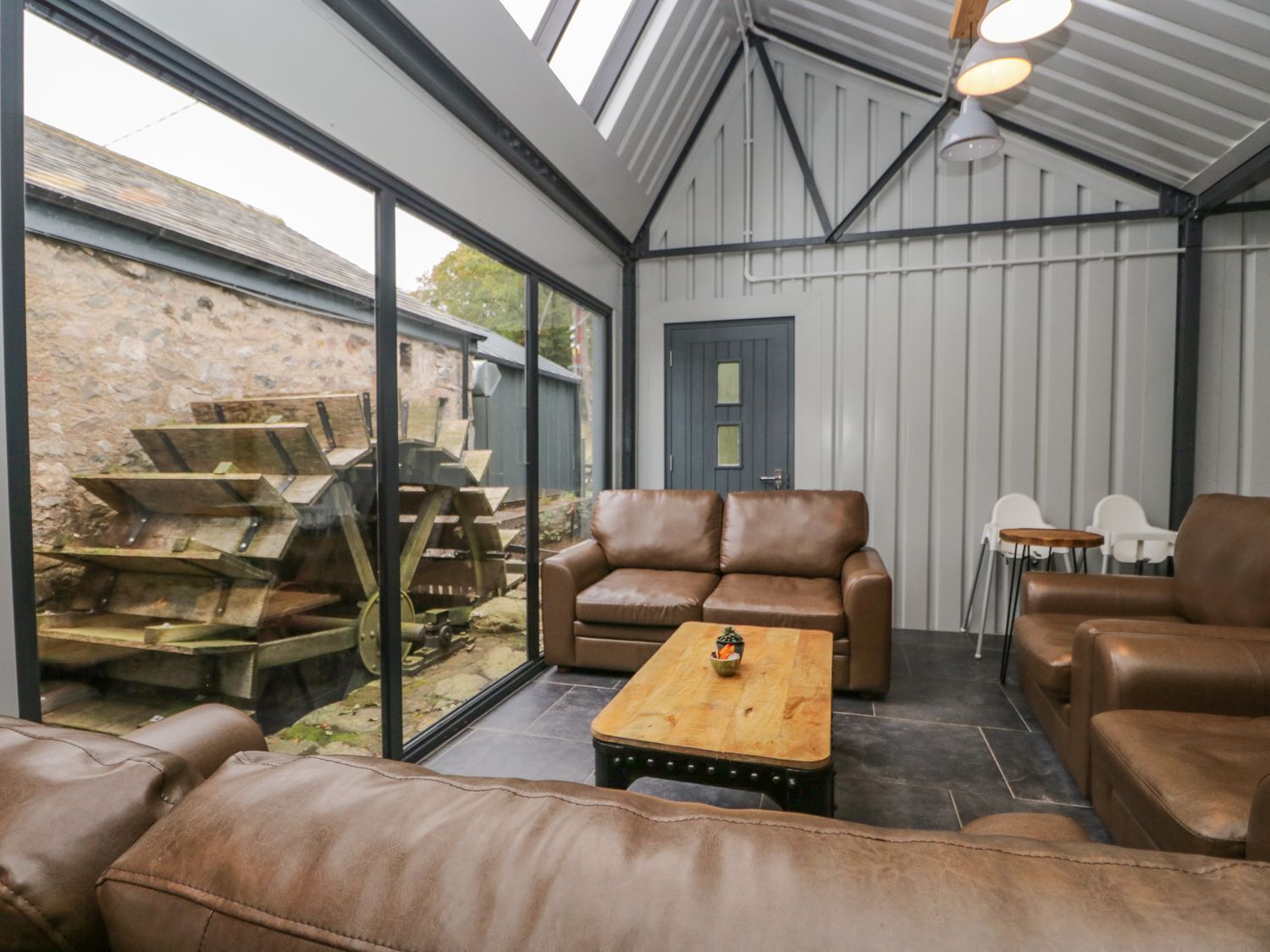A modern interior with leather sofas, a wooden coffee table, and a large glass window overlooking a stone wall and outdoor area.