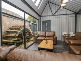 A modern interior with leather sofas, a wooden coffee table, and a large glass window overlooking a stone wall and outdoor area.